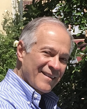 A photo of Steve Heikin. He is smiling at the camera and has light skin and silver hair. He is wearing a blue and white striped button-down shirt.